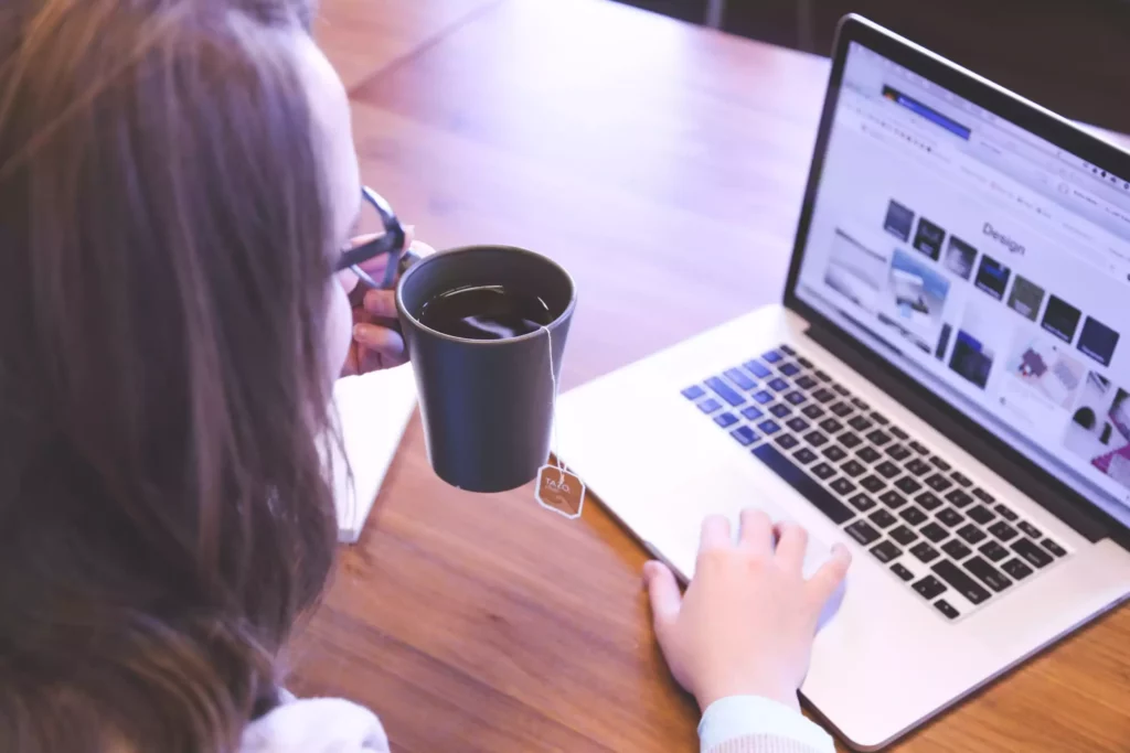 A person studying on a laptop while holding a hot beverage.